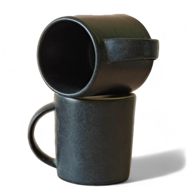 Display image of Matte black ceramic mug with a minimalist design and curved handle, placed on a white table.