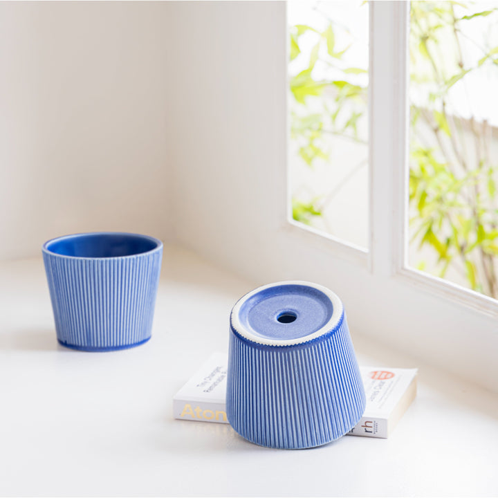 Two blue ceramic planters with textured patterns placed by a window, one turned upside down on top of a book, showcasing modern home decor elements.