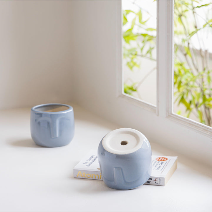 Display image of blue grey ceramic planter with a minimalist face design and a smooth matte finish.