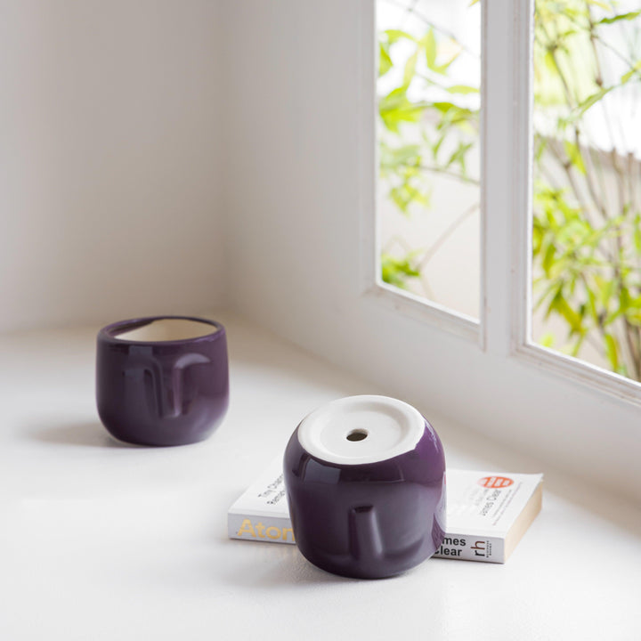 Display image of plum ceramic planter with a minimalist face design and a smooth matte finish.