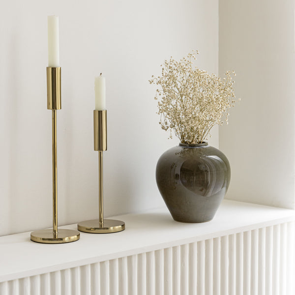 The Elegant Vase with dried flowers placed beside brass candle holders on a minimalist white shelf.